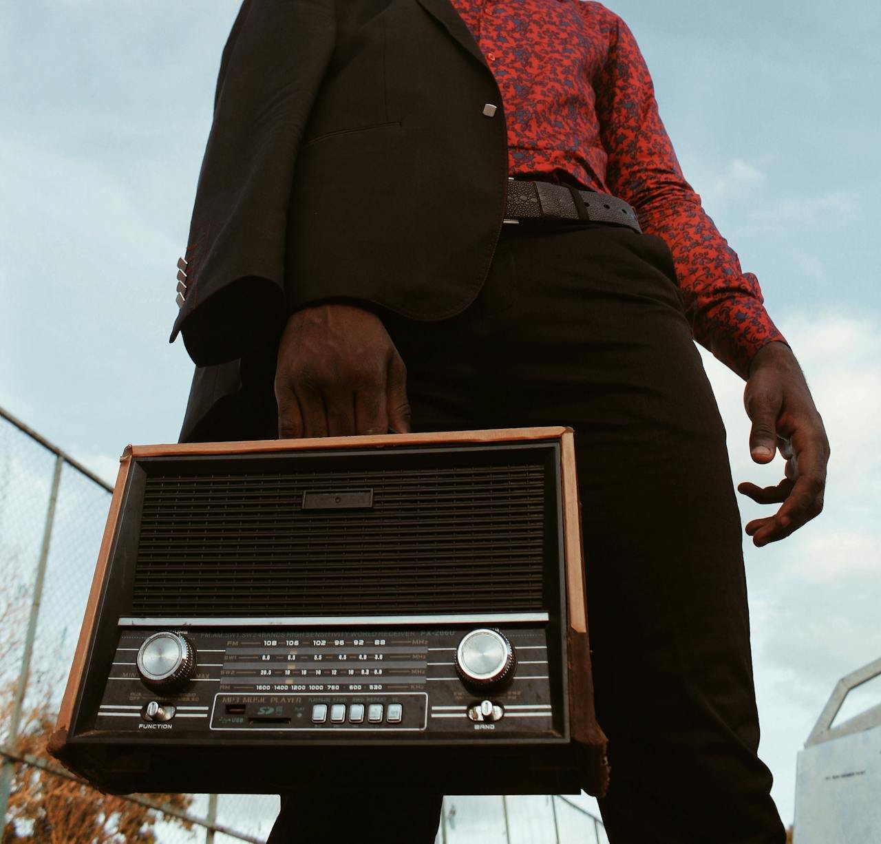 Man in vintage style holding a retro radio outdoors, low-angle shot.